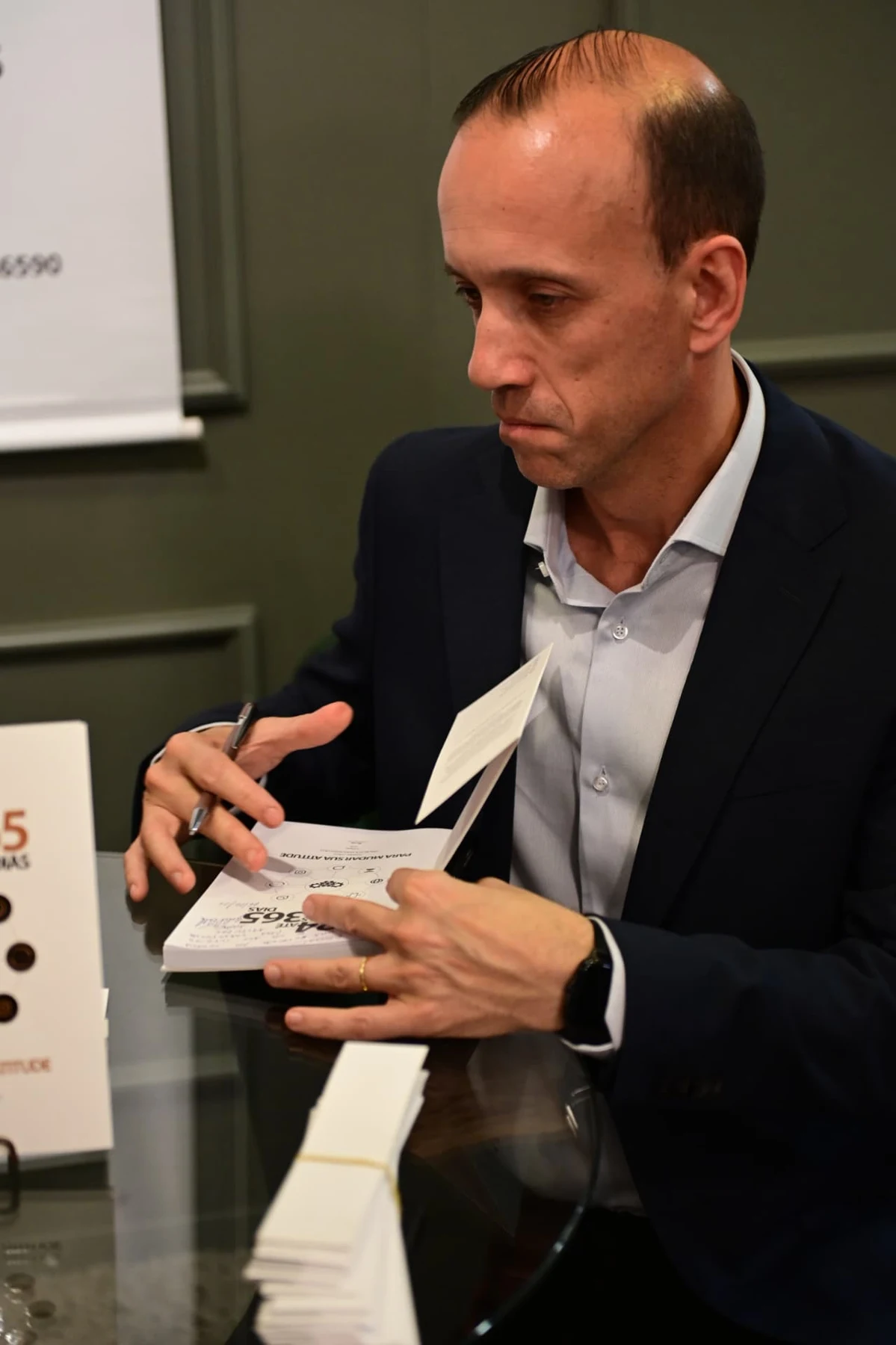 Gabriel com caneta e livro aberto durante a sessão de autógrafos